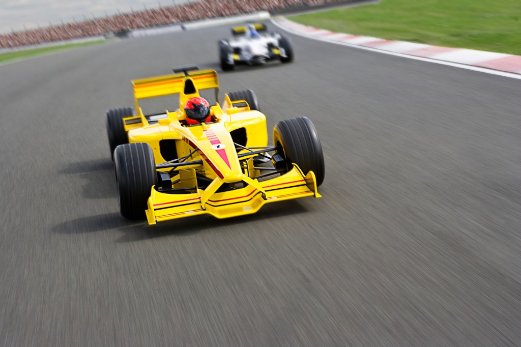 Two Formula One Racecars Racing Down Racetrack