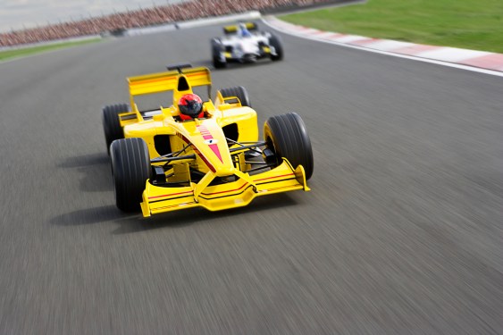 Two Formula One Racecars Racing Down Racetrack