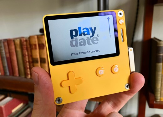 A Playdate handheld being held in a hand.