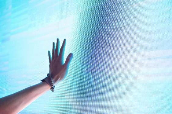 A raised left hand is pressing against an illuminated screen