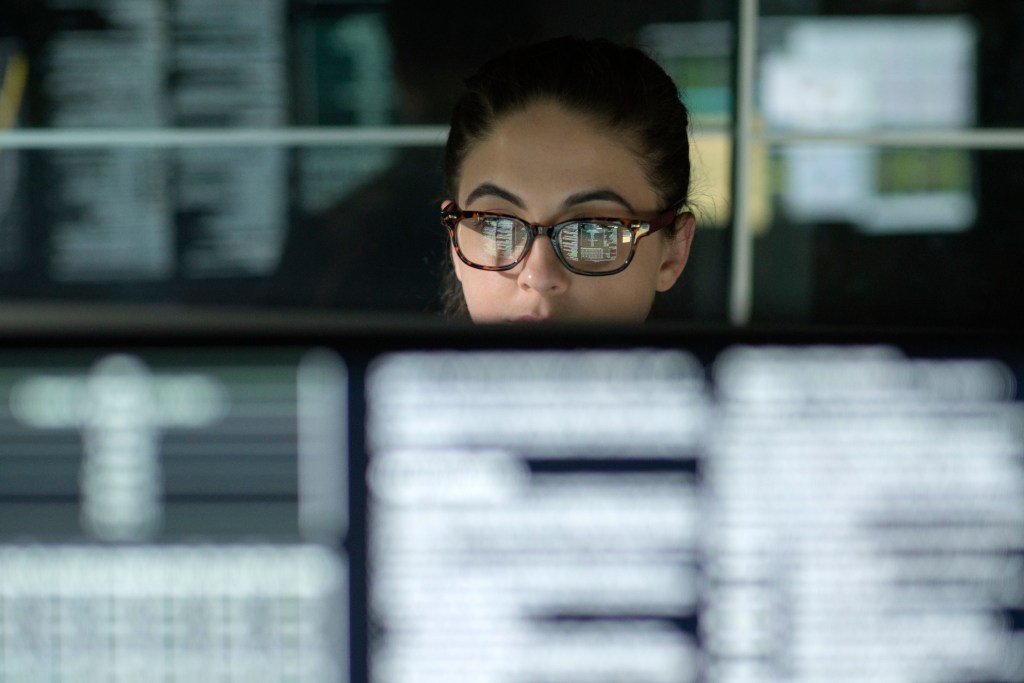 Image of a young woman surrounded by computer monitors.