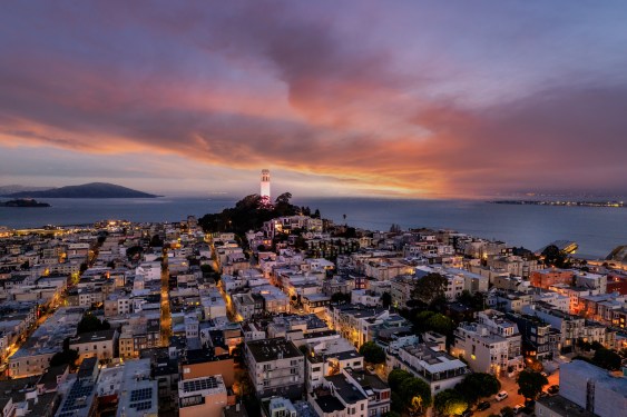 An aerial view of Coit Tower and the San Francisco Bay in the distance with a dramatic and vibrant sky.