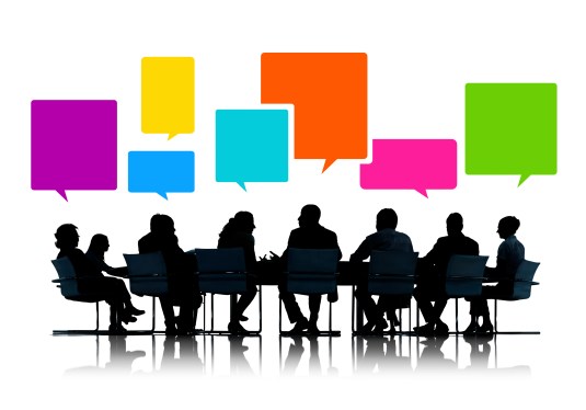 Silhouettes of businesspeople meeting at a table with multicolored speech bubbles above their heads.