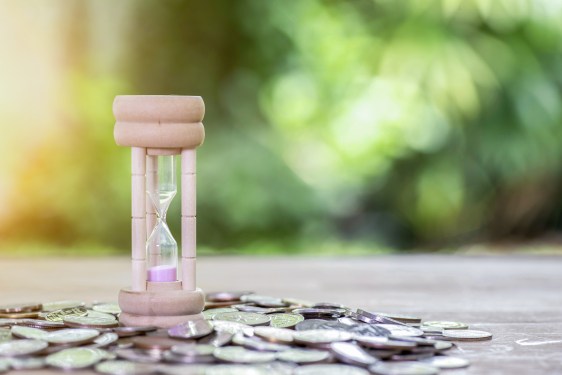 Image of an hourglass on top of a pile of coins.