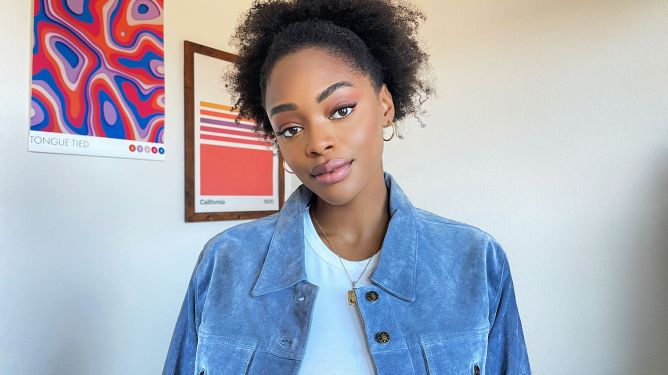 A Black woman smiles to the camera wearing pink lipstick