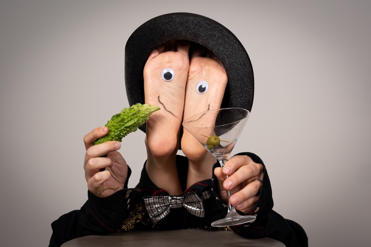 A pair of feet with a face on it, eating a pickle and drinking a cocktail