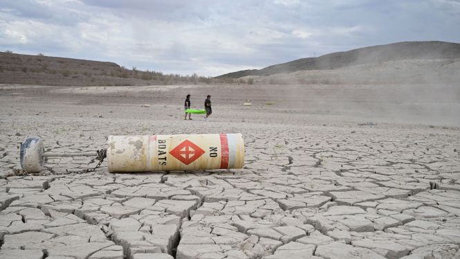 A buoy that reads 'No Boats' lays on cracked dry earth where water once was as people carry a boat further out to reach water at Lake Mead, Nevada on July 23, 2022.