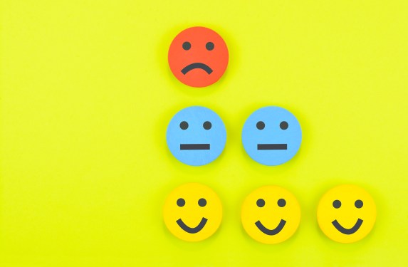 Image of one red sad face, two blue neutral faces, and three yellow smileys against a chartreuse background to represent feedback.
