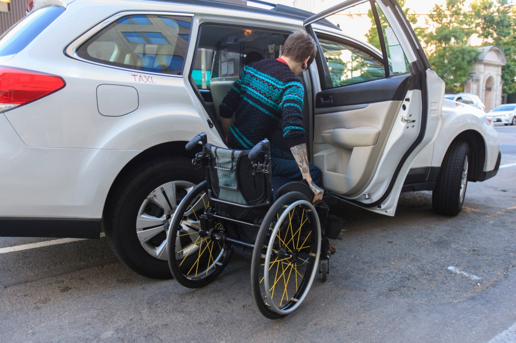 Trendy man with a spinal cord injury in wheelchair getting into a taxi cab