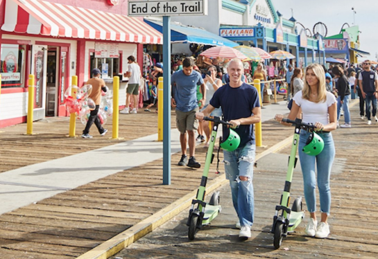 two young adults walking e-scooters