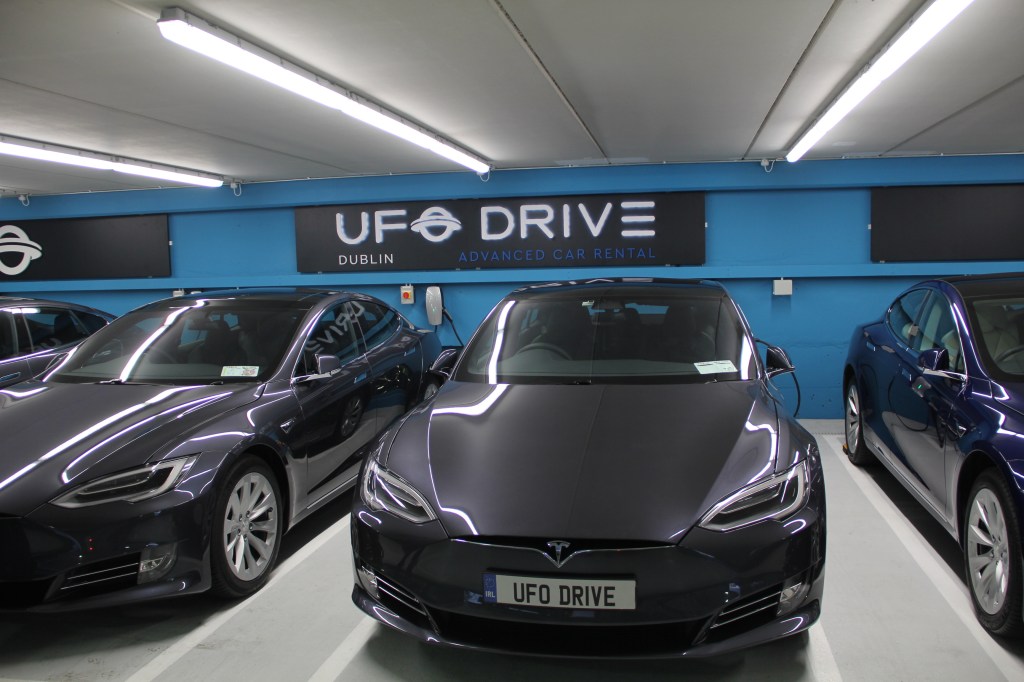 a row of black Teslas in front of UFODrive signage