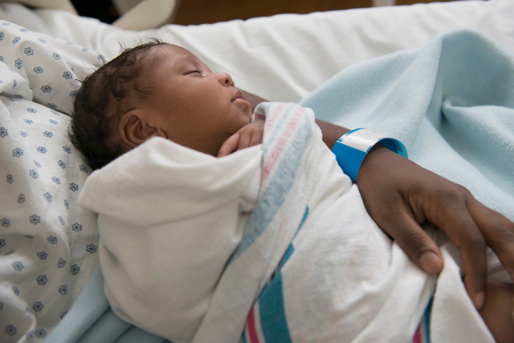 Newborn Black child in her mother's arms at the hospital, swaddled in a blanket.