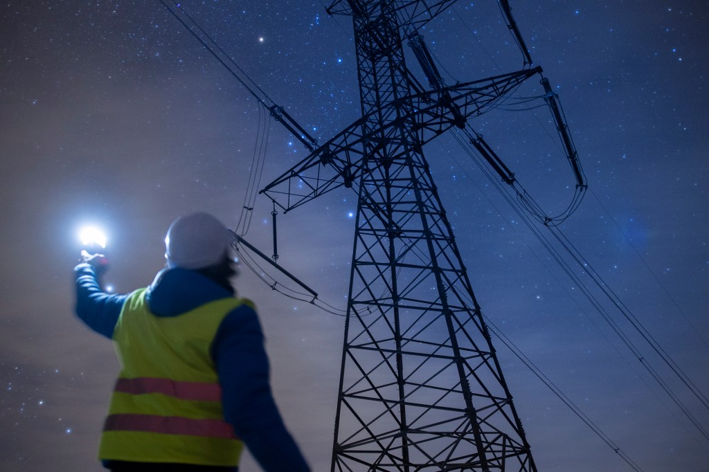 High-voltage engineer working on power lines at night.