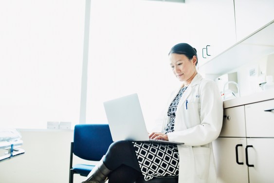 Portrait of female doctor working on laptop in exam room, used in a post about healthcare community Docquity