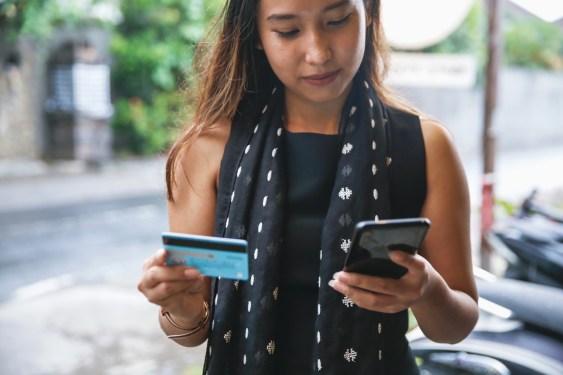Young Indonesian woman holding a credit card and smartphone, used in a post about credit tech startup SkorLife