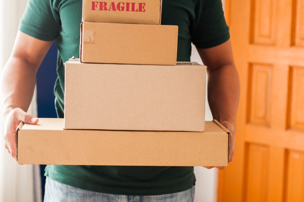 Front view midsection of Southeast Asian man holding stacks of carton packages indoor, used in post about Shipmates