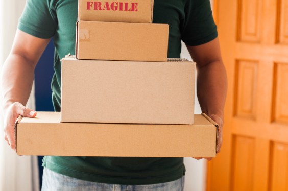 Front view midsection of Southeast Asian man holding stacks of carton packages indoor, used in post about Shipmates