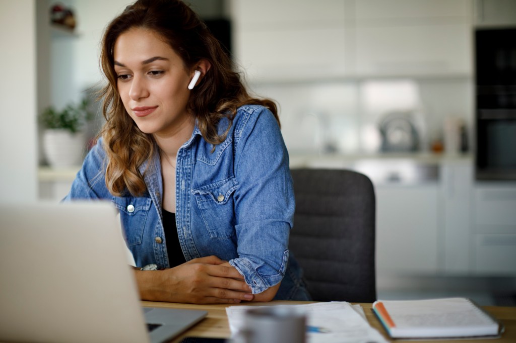 Young woman with bluetooth headphones having video conference at home, used in a post about meeting productivity app Loopin