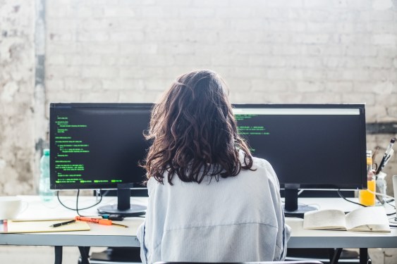 back of woman sitting at desk with two monitors