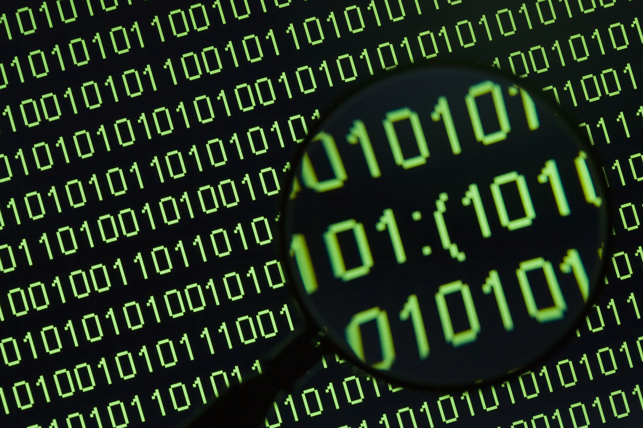 Magnifying glass showing word 'sad sign' in binary code on a computer display