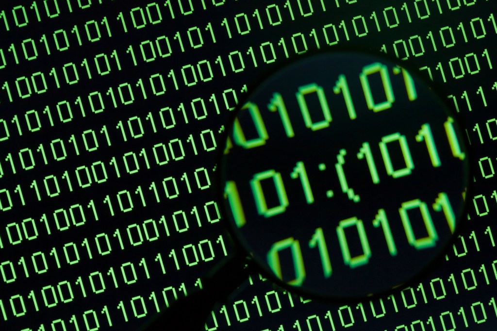 Magnifying glass showing word 'sad sign' in binary code on a computer display