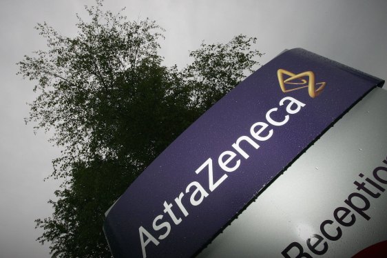 A darkened photo of a sign with the AstraZeneca logo on a purple background with a tree behind.