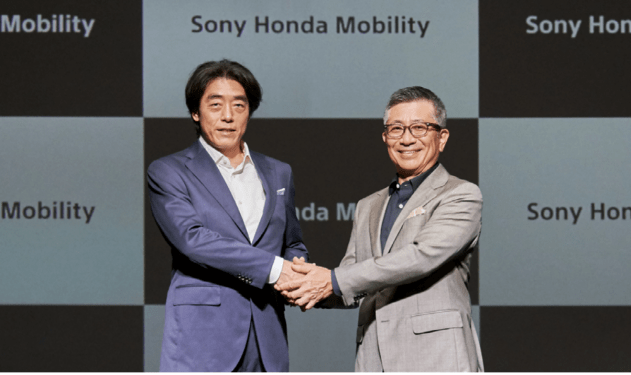 two men shaking hands under sony honda mobility sign