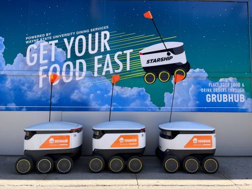 Three Starship sidewalk delivery robots with Grubhub logo under sign that says 'get your food fast'