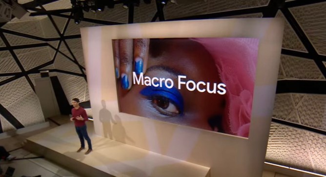A speaker on the Google stage from Made by Google Event 2022, with the words Macro Focus on a screen behind them