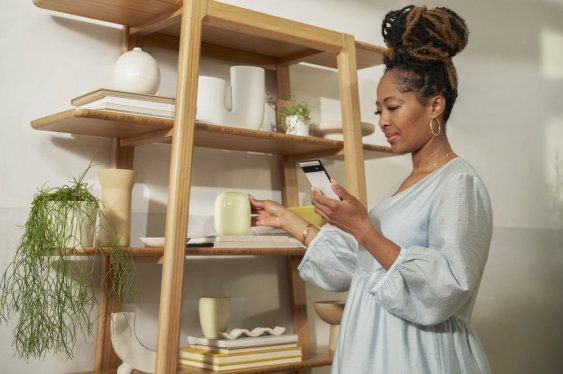 woman holding smartphone next to bookcase