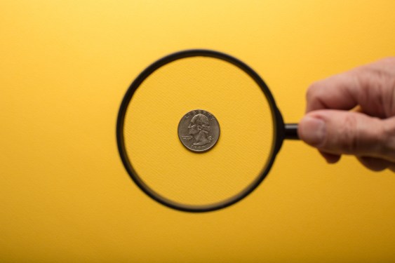 Human hand holding magnifying glass over american quarter on yellow background