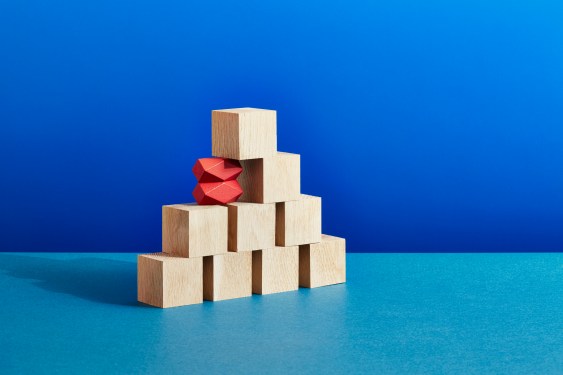 A stack of plain wooden blocks with two unusual red blocks supporting the edge