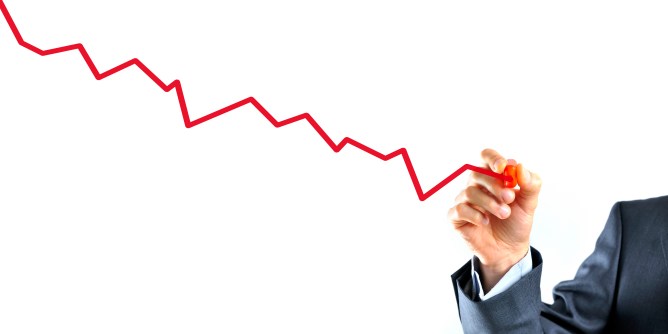 Closeup of businessman's hand drawing a graph with red line going down.