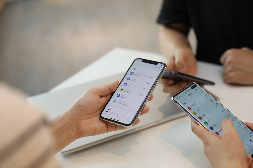 Three people, seated at table, holding cell phones.