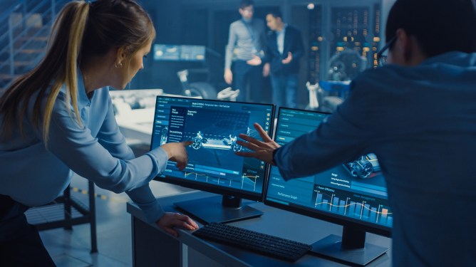 Man and woman engineers in front of a dual screen display designing an electric car.