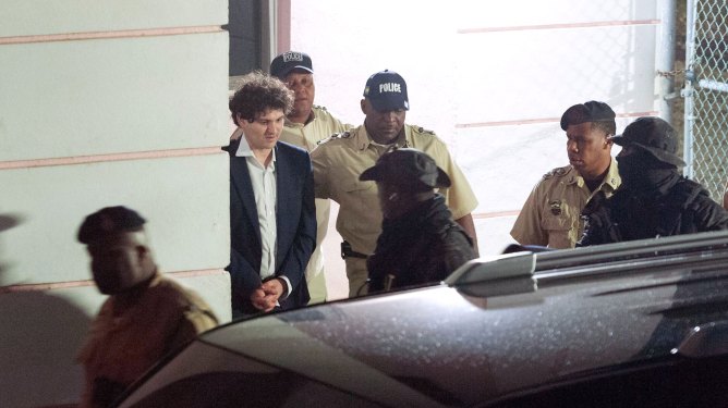 FTX founder Sam Bankman-Fried (2nd L) is led away handcuffed by officers of the Royal Bahamas Police Force in Nassau, Bahamas on December 13, 2022. - Disgraced cryptocurrency tycoon Sam Bankman-Fried was hit with multiple criminal charges December 13, 2022, accused of committing one of the biggest financial frauds in US history. Bankman-Fried will serve time at The Bahamas Department of Corrections until February 8, 2023. (Photo by Mario DUNCANSON / AFP) (Photo by MARIO DUNCANSON/AFP via Getty Images)