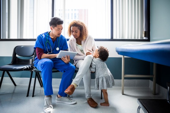 Male nurse showing digital tablet to mother by toddler in hospital, used in a post about Ubie