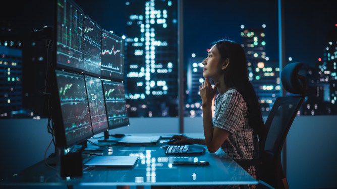 Portrait of a Financial Analyst Working on Computer with Multi-Monitor Workstation with Real-Time Stocks, Commodities and Exchange Market Charts. Businesswoman at Work in Investment Broker Agency, used in a post about WritePath