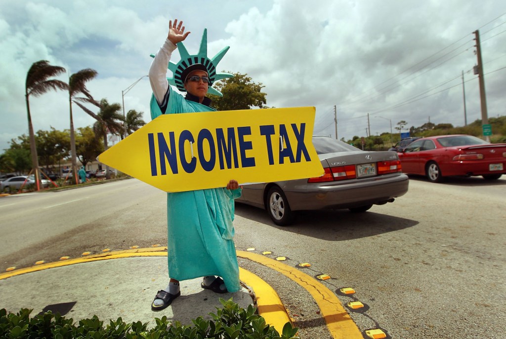 A person dressed as the Statue of Liberty holding a yellow sign that says "INCOME TAX"