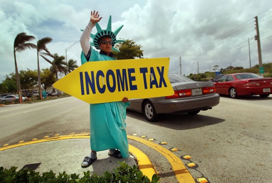 A person dressed as the Statue of Liberty holding a yellow sign that says "INCOME TAX"