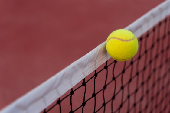 Tennis ball hitting the net on red court.