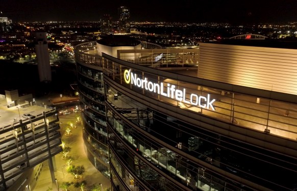a snapshot of a flyover of the top of Norton Lifelock's offices at night with a city silhouette in the background
