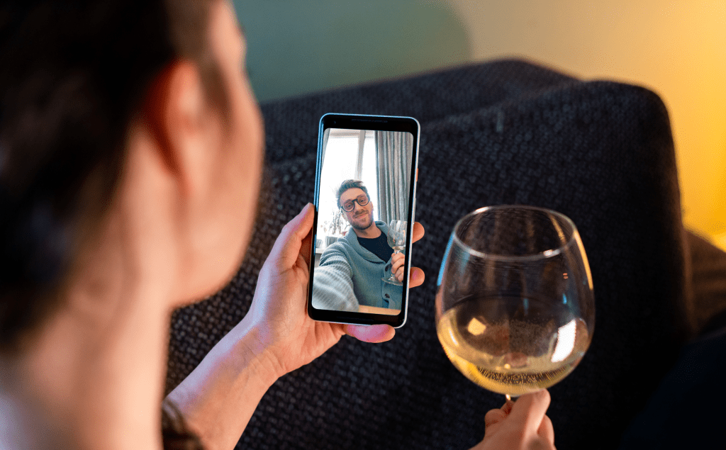 video chat date; woman holding glass of wine and smartphone