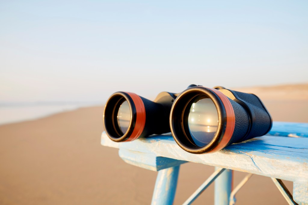 Close-up of binoculars on table by the sea during sunset, the sunset is reflected in the glass of the binoculars