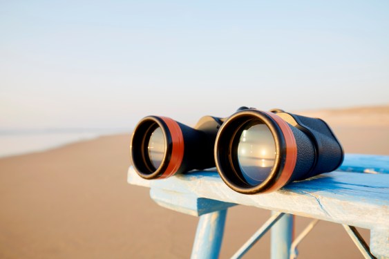 Close-up of binoculars on table by the sea during sunset, the sunset is reflected in the glass of the binoculars
