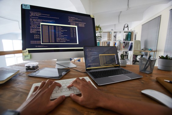 Developer coding at desk with laptop and large second monitor.