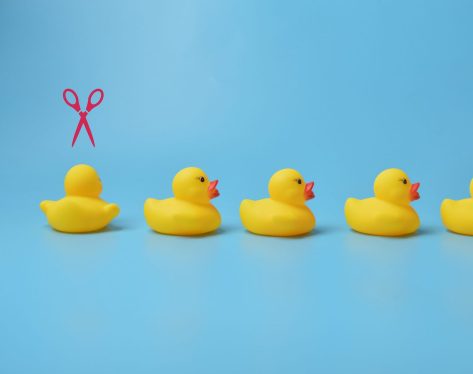 Pink scissors pointing to toy duck. Firing, unemployment, job losses and economy crisis concept.