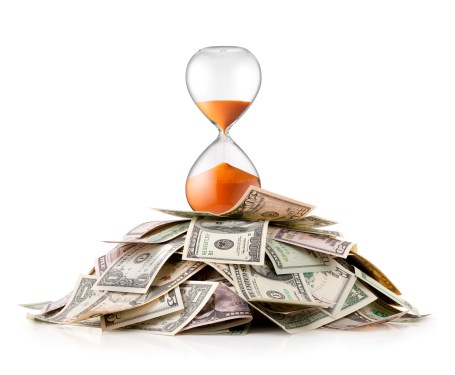 Image of a pile of money with an hourglass atop it.