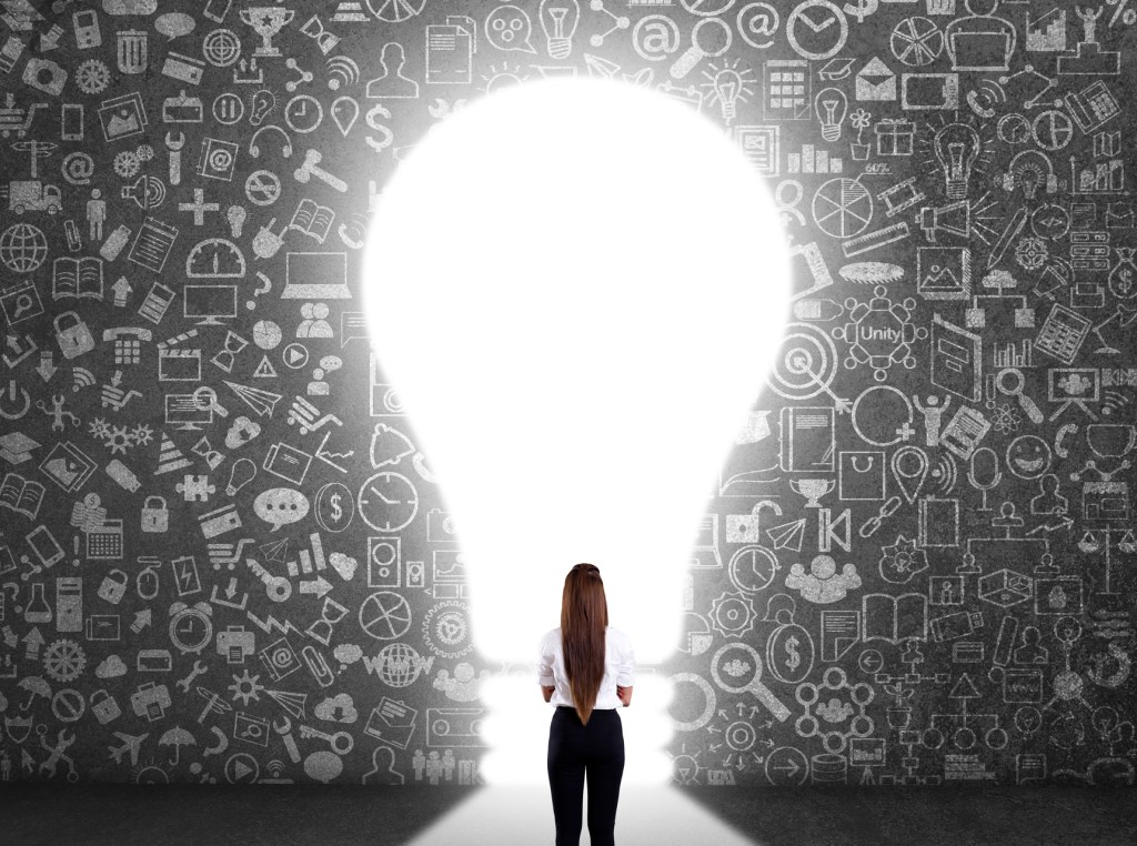Concept of woman standing in front of a wall of ideas with a light bulb entrance, as she considers the viability of her startup idea