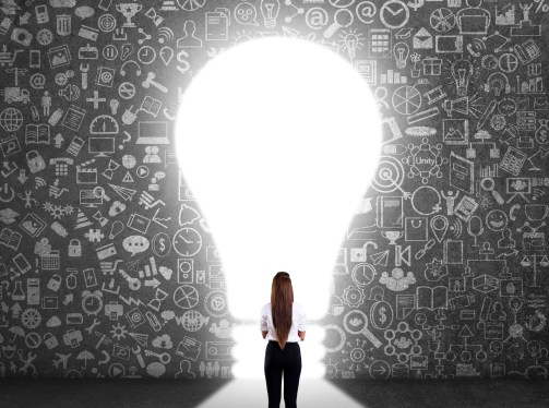 Concept of woman standing in front of a wall of ideas with a light bulb entrance, as she considers the viability of her startup idea